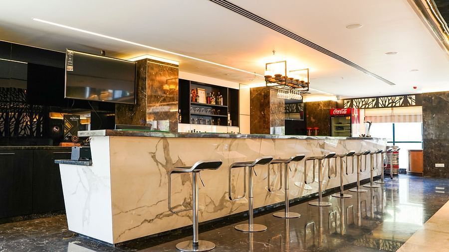A sleek and modern bar area at BNGV Grandeur Hotel and Banquets, featuring a long counter with multiple high stools and elegant lighting.