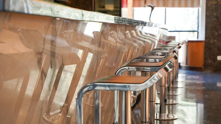 A detailed close-up of a warm-toned wooden bar counter with several bar stools at BNGV Grandeur Hotel and Banquets, highlighting the texture and design.