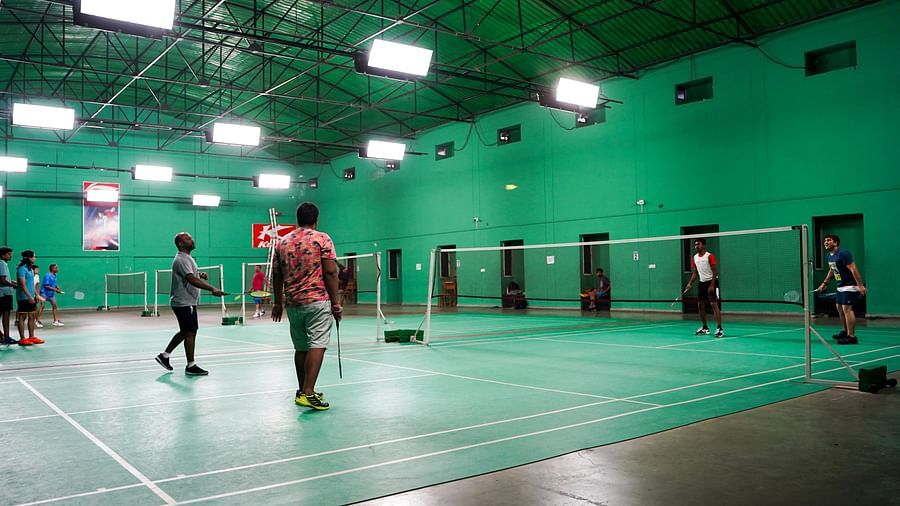An indoor badminton court with green flooring, showing people playing at BNGV Grandeur Hotel and Banquets.