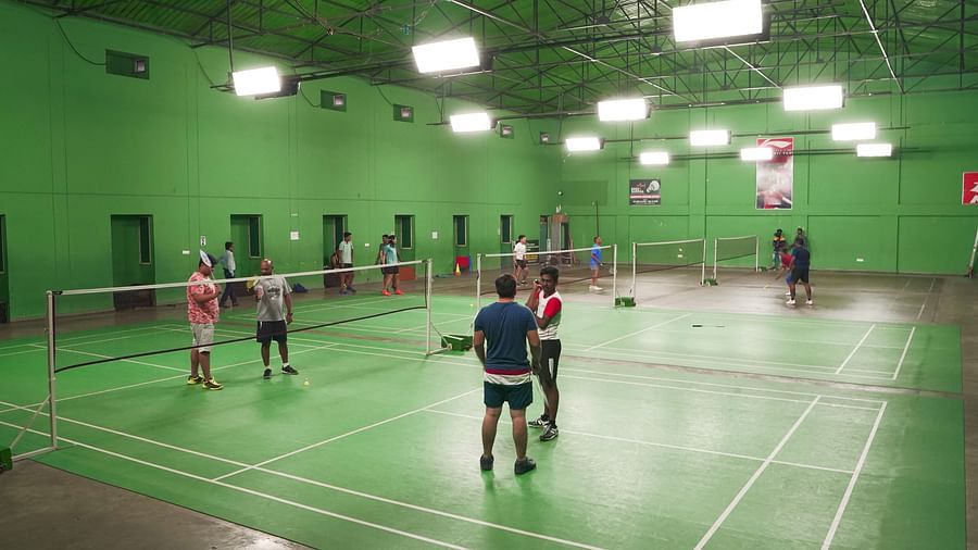 Another view of an indoor badminton court with green flooring, showing players in action at BNGV Grandeur Hotel and Banquets.
