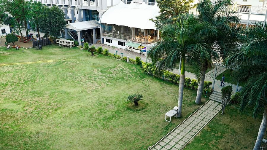 An aerial view of the lush green lawns and exterior of BNGV Grandeur Hotel and Banquets, surrounded by palm trees.