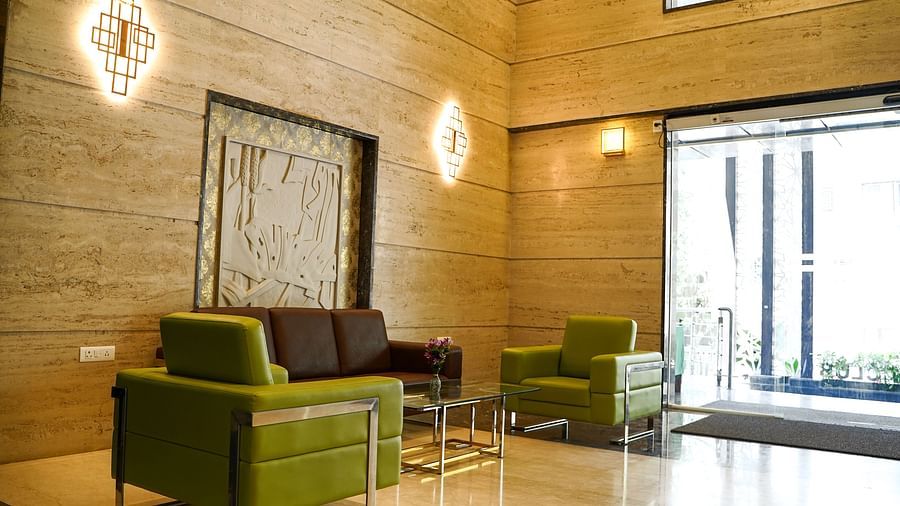 A bright and spacious lounge area at BNGV Grandeur Hotel and Banquets with green armchairs and a brown sofa, leading to an open doorway.
