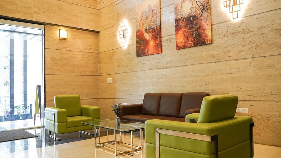 A comfortable seating arrangement in the lobby of BNGV Grandeur Hotel and Banquets, featuring green armchairs and a brown sofa, with decorative wall art.