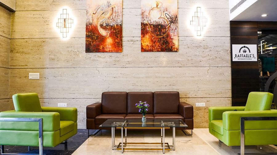 A hotel lobby seating area at BNGV Grandeur Hotel and Banquets with green armchairs, a brown sofa, and abstract art on the wall.
