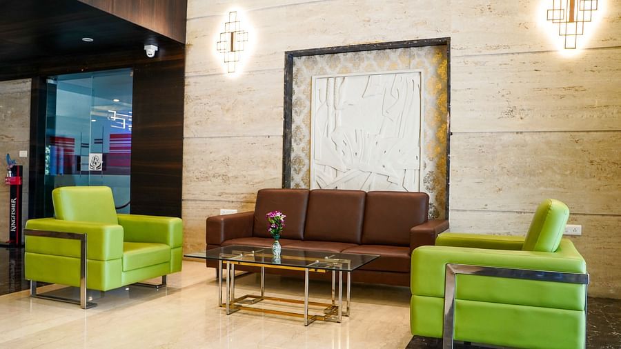 An inviting lounge area at BNGV Grandeur Hotel and Banquets with green armchairs, a brown sofa, and contemporary lighting fixtures.