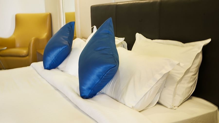 A close-up view of the comfortable bed in a hotel room at BNGV Grandeur Hotel and Banquets, highlighting the plush white pillows with decorative blue accents.