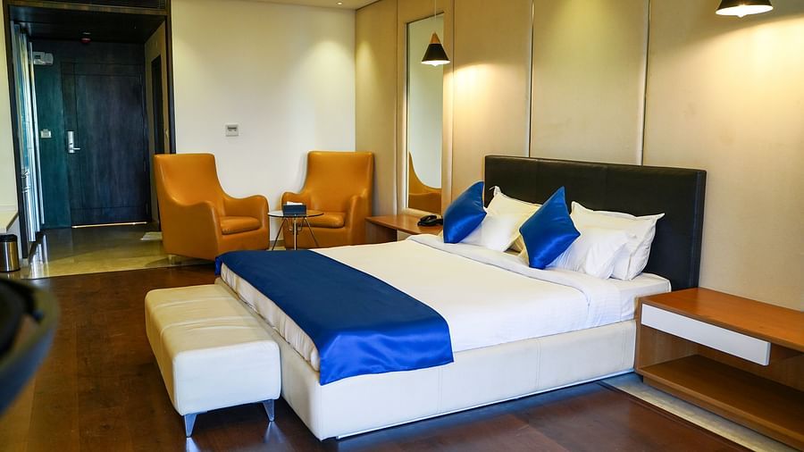 A stylish hotel room at BNGV Grandeur Hotel and Banquets, equipped with a bed featuring a dark headboard and blue accents, complemented by two vibrant orange armchairs.