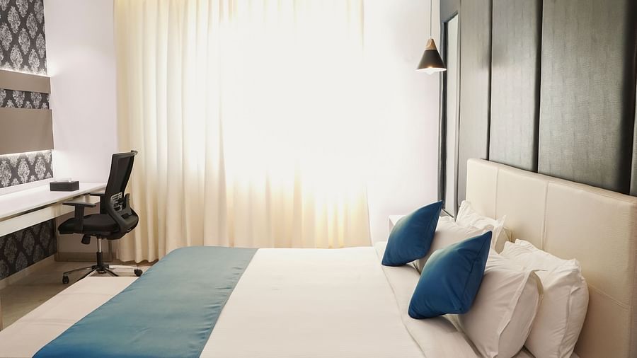 A contemporary hotel room at BNGV Grandeur Hotel and Banquets, offering a comfortable bed, a functional desk with a chair, and sleek, minimalist decor.