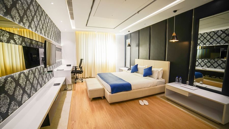 A modern and elegantly designed hotel room at BNGV Grandeur Hotel and Banquets, featuring a comfortable bed with a blue runner, a unique patterned accent wall, and contemporary furnishings.