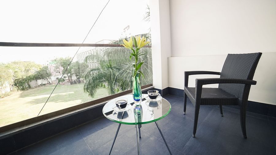 A bright balcony space at BNGV Grandeur Hotel and Banquets with an outdoor chair and a small glass table, offering a view of the surrounding greenery.