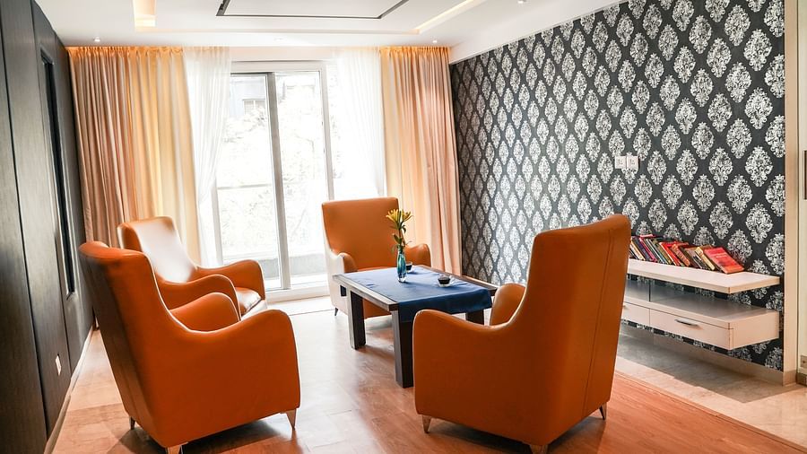 A stylish living area at BNGV Grandeur Hotel and Banquets, featuring comfortable orange armchairs, a coffee table, and a contemporary patterned accent wall.
