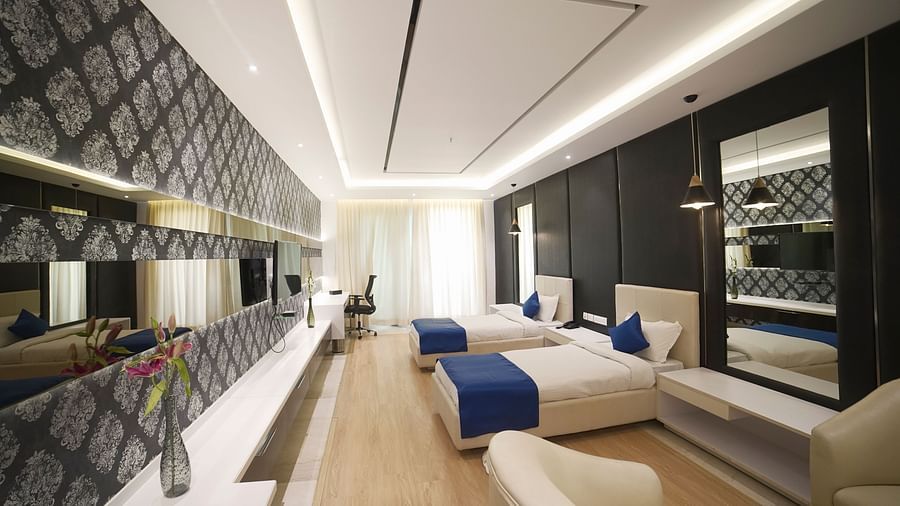  A stylish hotel room at BNGV Grandeur Hotel and Banquets, showcasing a bed with a blue runner, a patterned accent wall, and well-designed lighting.