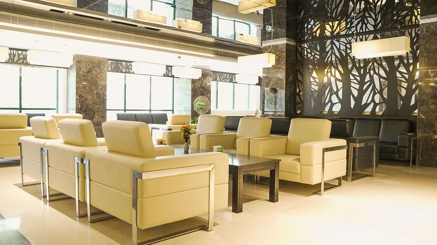 A broad view of a luxurious lounge at BNGV Grandeur Hotel and Banquets, featuring contemporary light-coloured seating, dark decorative wall panels, and natural light from large windows.