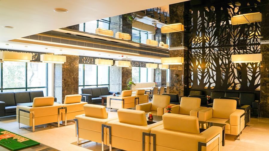 A cosy dining area at BNGV Grandeur Hotel and Banquets with comfortable dark sofas and armchairs, bathed in warm lighting from a window.
