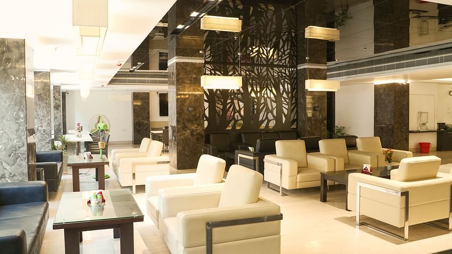 A sophisticated lounge area at BNGV Grandeur Hotel and Banquets with comfortable light-coloured seating, square tables, and a striking reflective ceiling design.