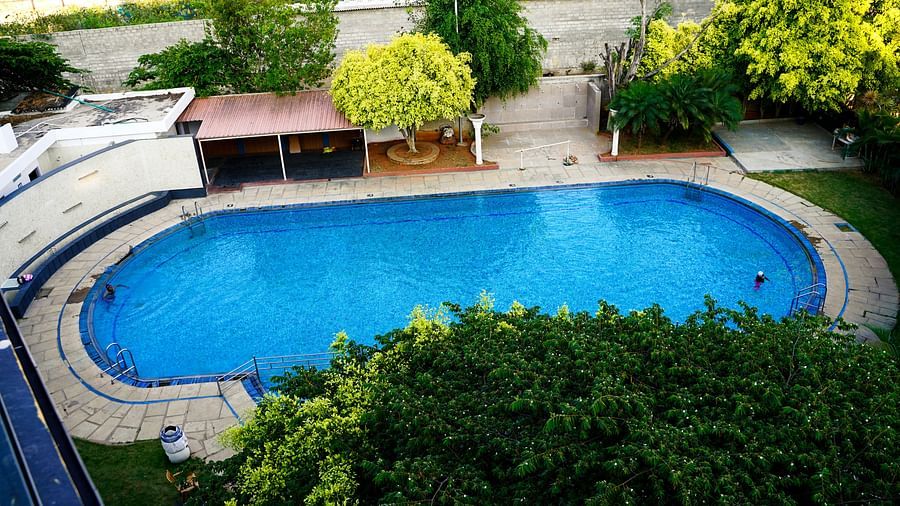 An aerial view of a large, inviting outdoor swimming pool at BNGV Grandeur Hotel and Banquets, surrounded by lush green trees.