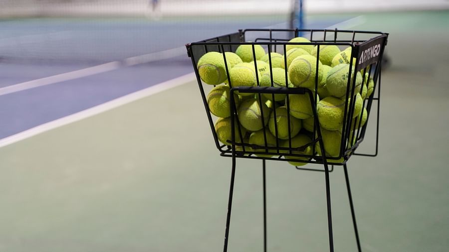A black wire basket filled with green tennis balls, positioned on a tennis court at BNGV Grandeur Hotel and Banquets.