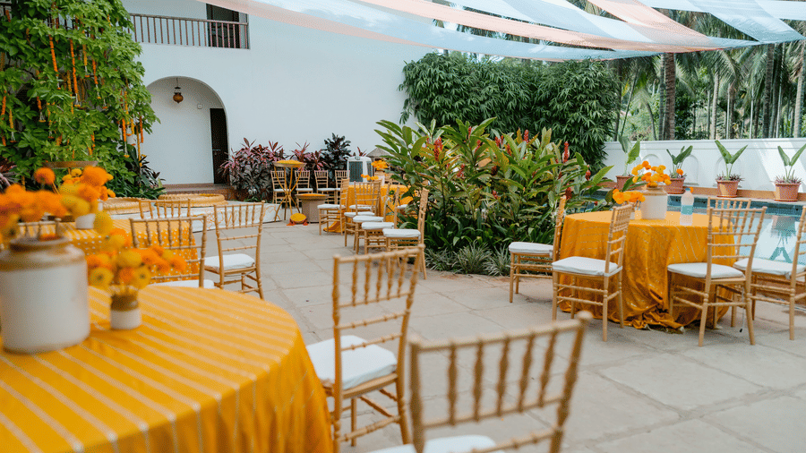 Round dining tables with bright tablecloths, wooden chairs, floral centrepieces at Bougainvillea, Alibaug.