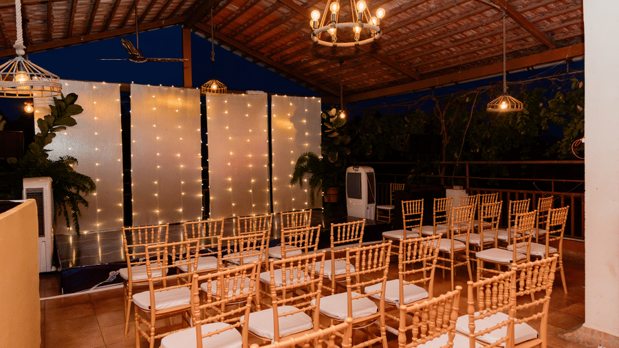 An indoor event space set up with rows of wooden chairs, a lighted backdrop, a hanging chandelier at Bougainvillea, Alibaug.