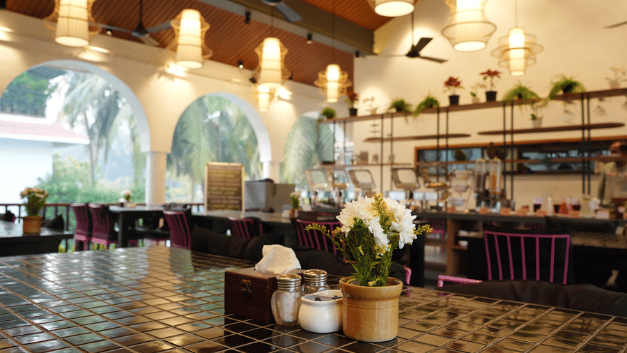 Tiled tables, pink chairs, and unique hanging lamps decorate an indoor restaurant space at Bougainvillea, Alibaug.