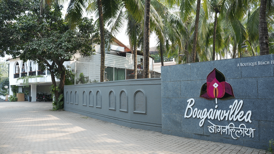 A stone entrance wall featuring a logo, the name Bougainvillea, and palm trees at Bougainvillea, Alibaug.