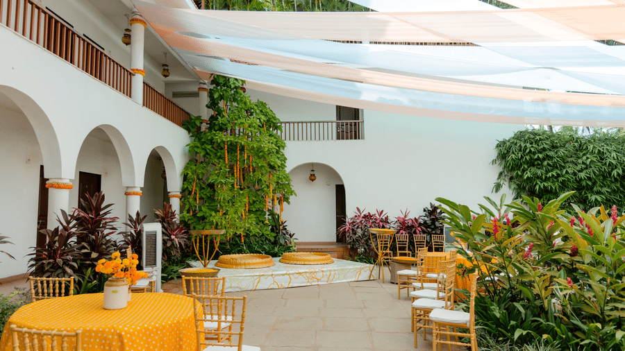An outdoor event venue decorated with draped fabric canopies, round tables, wooden chairs at Bougainvillea, Alibaug.