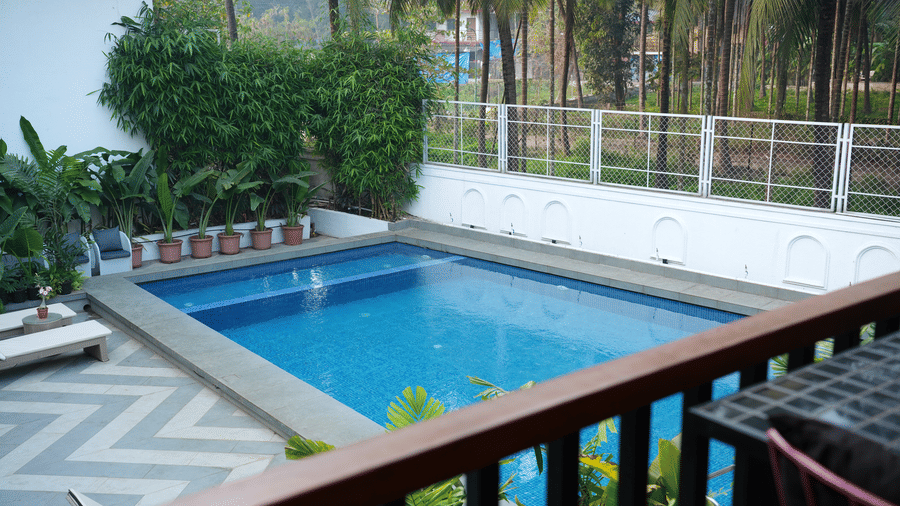 A swimming pool, sun loungers, and a paved deck are viewed from an elevated balcony at Bougainvillea, Alibaug.