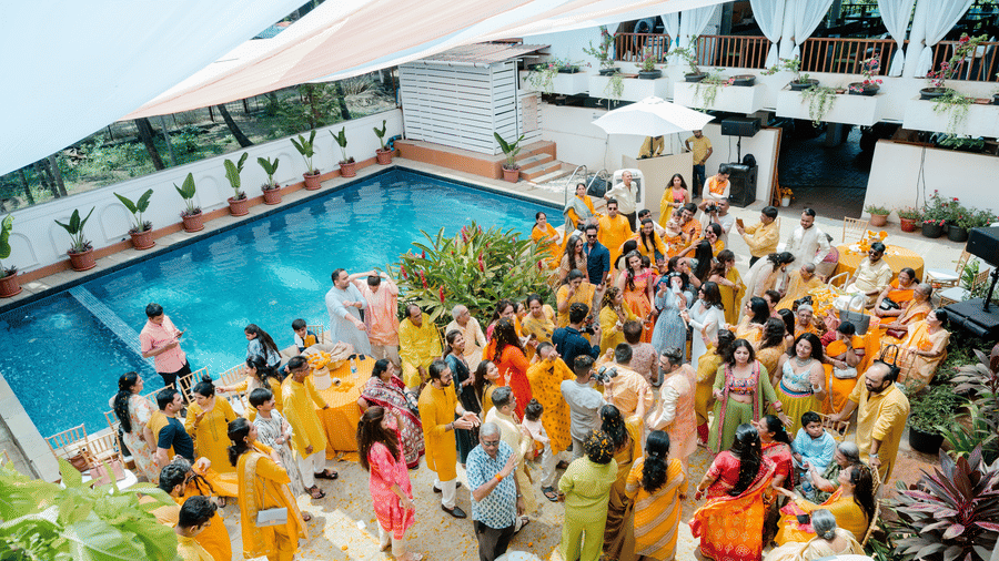A large crowd of people celebrates around a swimming pool, tables, and under a canopy at Bougainvillea, Alibaug.
