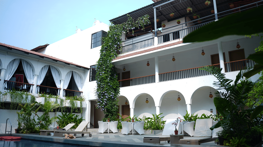 A multi storey white building overlooks a swimming pool, featuring arched corridors, climbing vines, balconies at Bougainvillea, Alibaug.