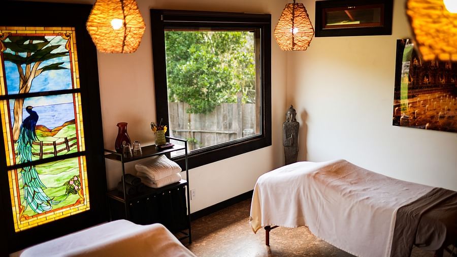 A massage room with soft lighting, white linens, and a window overlooking lush greenery - Brewery Gulch Inn & Spa