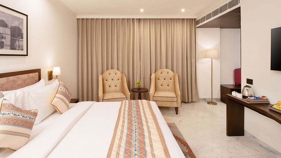 An image of a bedroom with bedside table, photo frame hanged on the wall, work desk with sofa chair, and a flat TV screen - Brij Eternity, Vrindavan