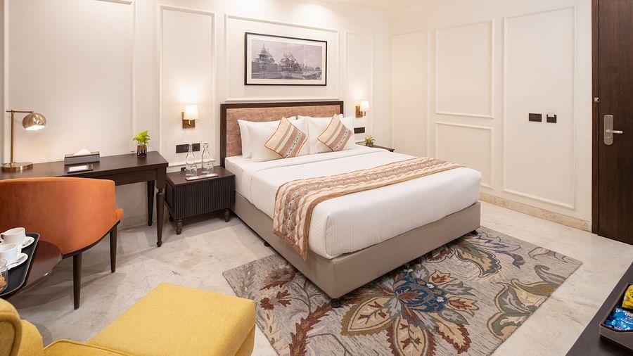 An image of a bedroom with bedside table, photo frame hanged on the wall, work desk with sofa chair, and a flat TV screen - Brij Eternity, Vrindavan