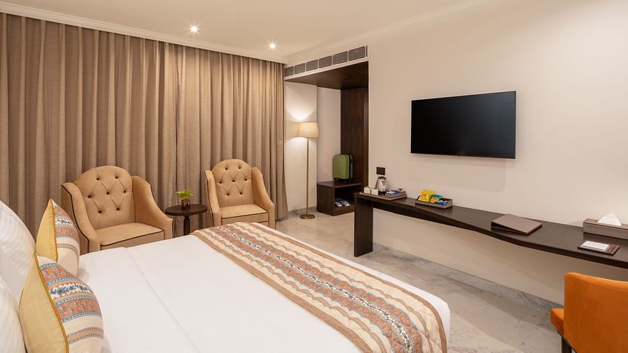 An image of a bedroom with bedside table, photo frame hanged on the wall, work desk with sofa chair, and a flat TV screen - Brij Eternity, Vrindavan
