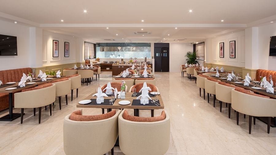 An image of a dining space with sofa chairs, centre table with hand towels and cutlery, and a buffet served at one corner - Brij Eternity, Vrindavan