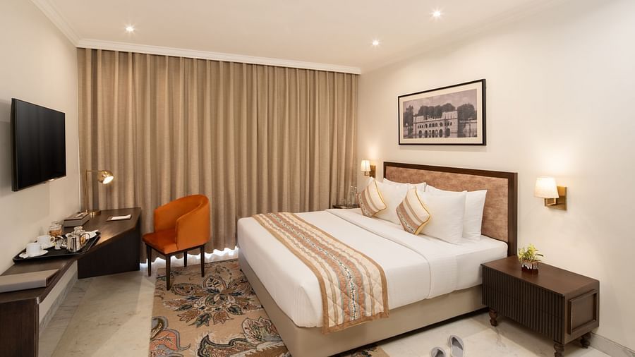 An image of a bedroom with bedside table, photo frame hanged on the wall, work desk with sofa chair, and a flat TV screen - Brij Eternity, Vrindavan