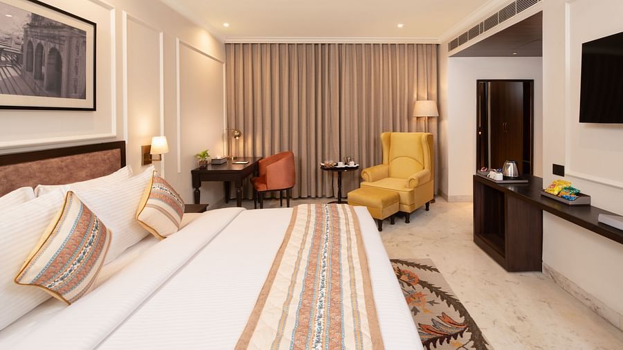 An image of a bedroom with bedside table, photo frame hanged on the wall, work desk with sofa chair, and a flat TV screen - Brij Eternity, Vrindavan
