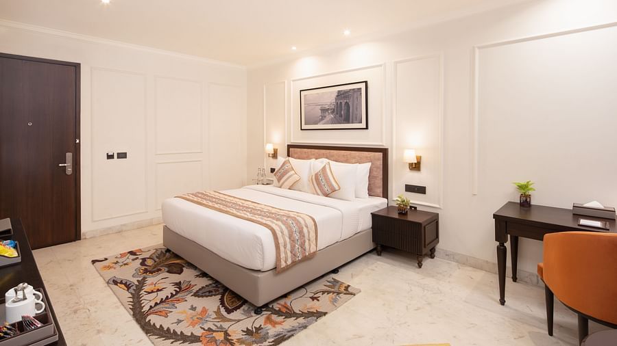 An image of a bedroom with bedside table, photo frame hanged on the wall, work desk with sofa chair, and a flat TV screen - Brij Eternity, Vrindavan