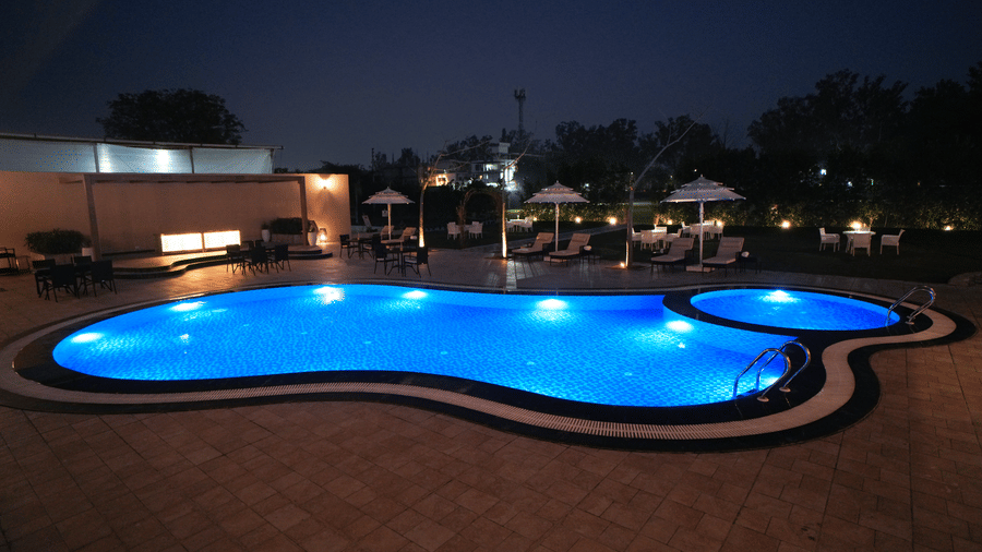Curved outdoor pool at Brij Eternity Vrindavan glowing at dusk with lounge chairs, umbrellas and open courtyard ambience