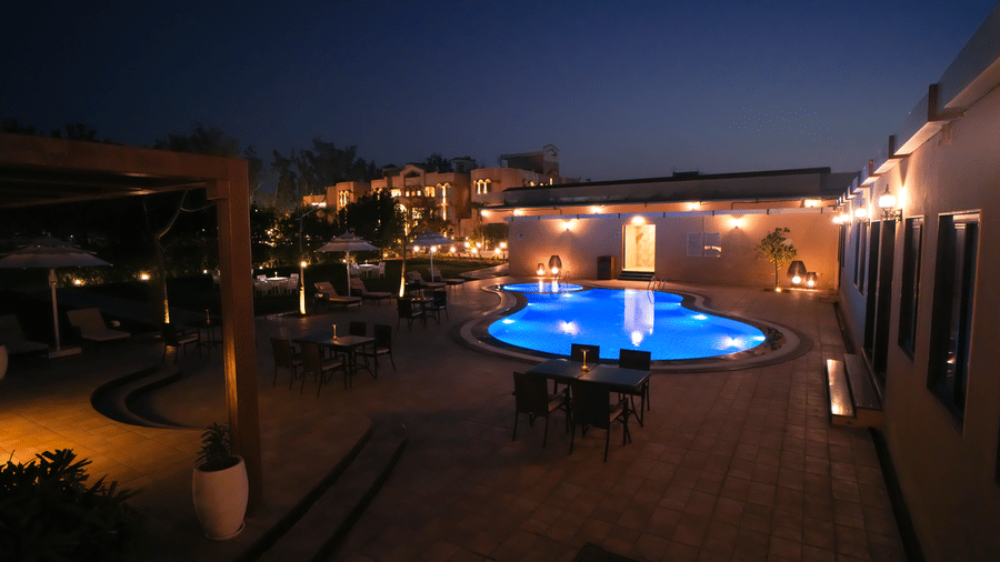 Night view of illuminated swimming pool at Brij Eternity Vrindavan with surrounding seating, warm lighting and tranquil courtyard setting