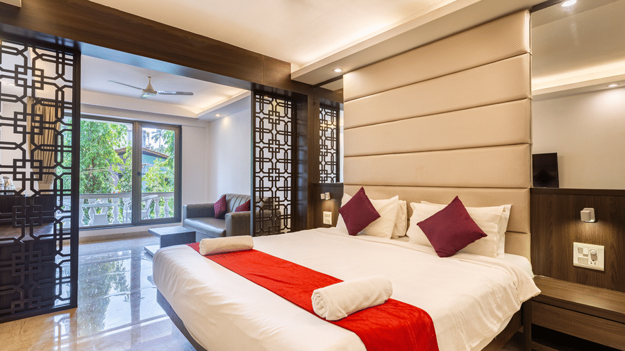Room with a plush bed, red accents, and a cozy seating area at CALUX Joia Do Mar Resort, Goa, filled with warm natural light