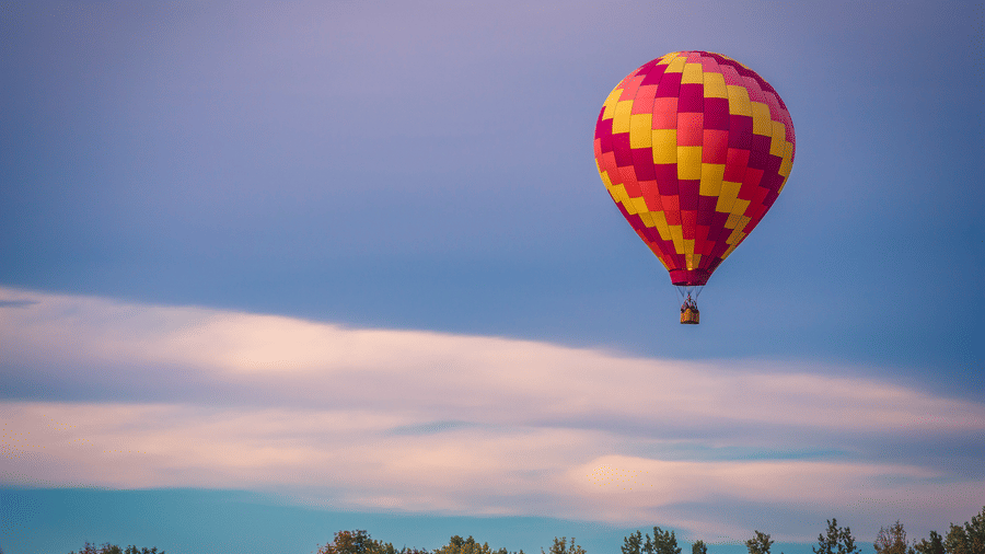 A lone hot air balloon high in the sky with clouds in the background