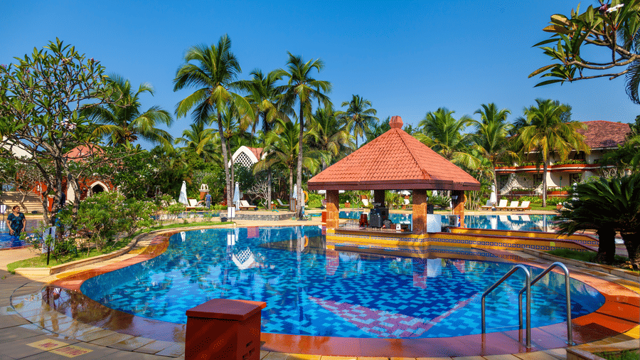 overview of the swimming pool with trees in the background - Caravela Beach Resort Goa