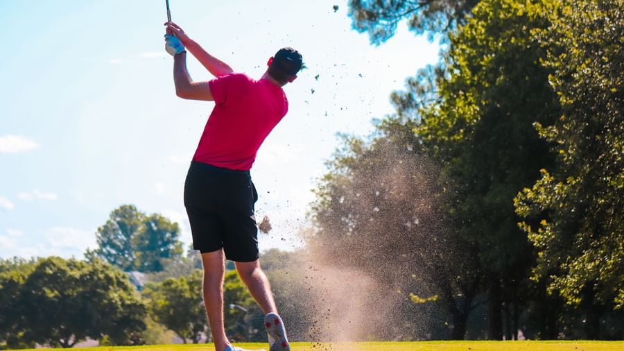 A golfer in mid-swing, hitting the ball with power and precision on a sunny day, surrounded by lush greenery.