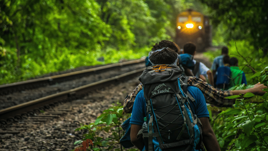 a group of people walking on the side of a train track and a train on-coming on the same track