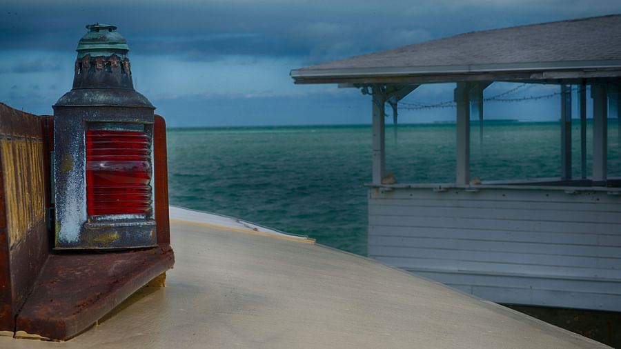 A red lantern on a wooden walkway at Casa Morada, with a white overwater structure and ocean view in the background.