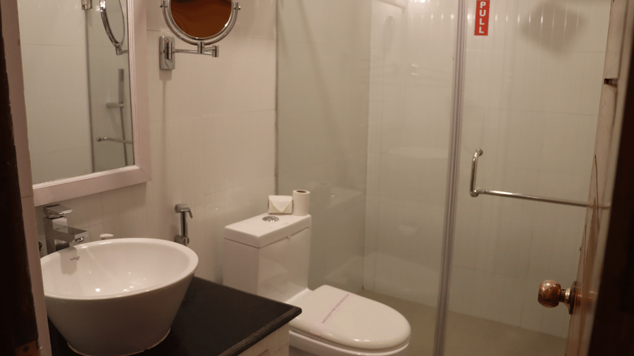 Compact bathroom with wall-mounted toilet, pedestal sink, and frameless glass shower door, tiled walls at Cedar Inn.