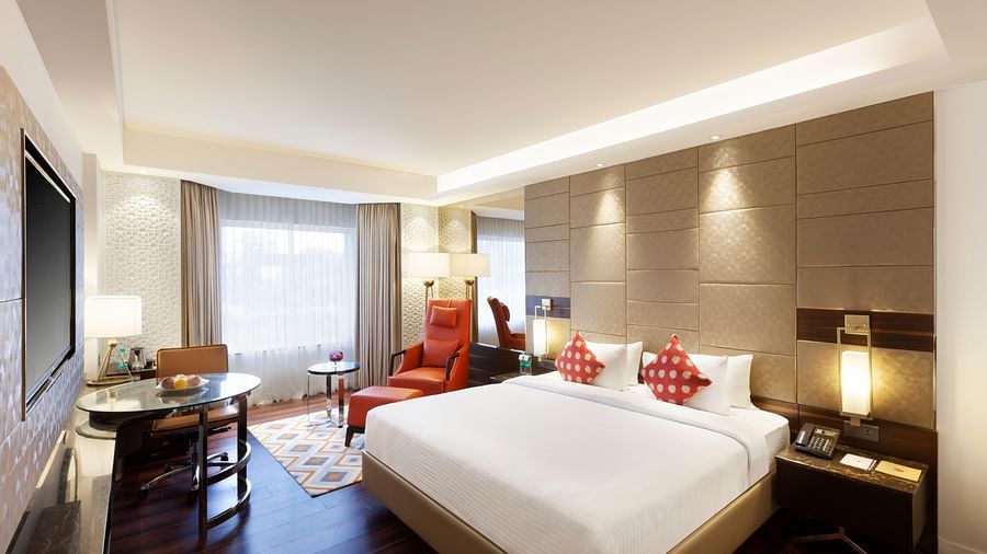 A spacious room with a large bed, wall-mounted TV, table, and cushioned chair, with curtains pulled to the side of the windows | Cenneys Gateway