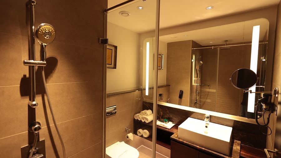 A spacious washroom with a glass panel separating the shower area from the Western toilet and a washbasin below the wall-mounted mirror | Cenneys Gateway