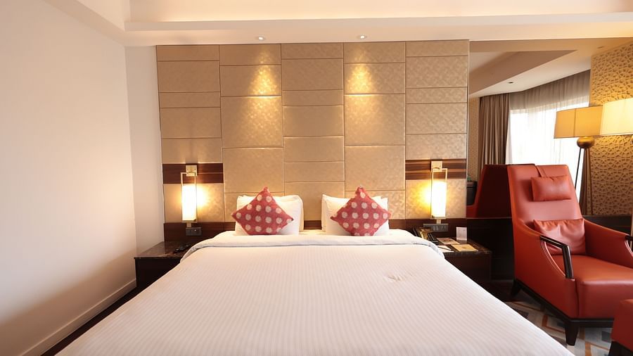 A front view of a spacious bed with bedside tables and lamps on both sides, and a cushioned chair on one side | Cenneys Gateway