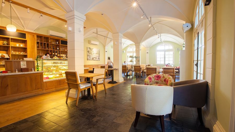 A cafe with tables and chairs, and a long counter with display shelves | The Shop | Central Mansions, Phnom Penh